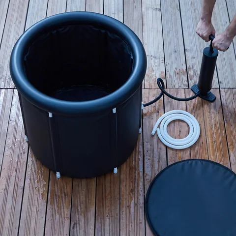 The kit's accessories laid out on cedar deck boards: the black carry bag, six white support tubes, a black hand pump, a white drain hose with its valve, the black water cushion and the padded lid.