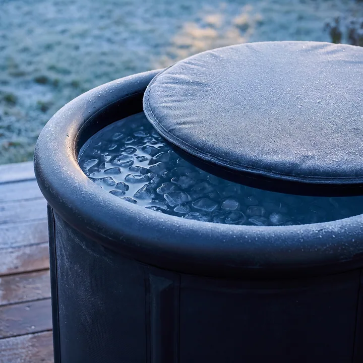 Close-up of the padded lid of the Ice Bath Tub slid half open on the top ring, frost on the lid and icy water underneath